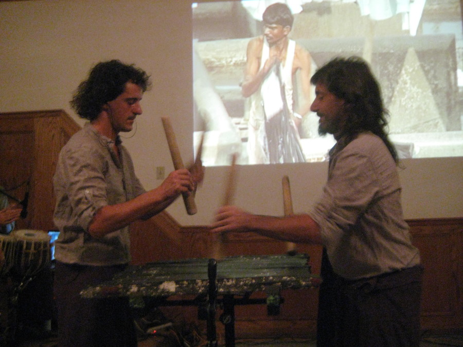 Two men hold thick wooden sticks and hit the txalaparta board